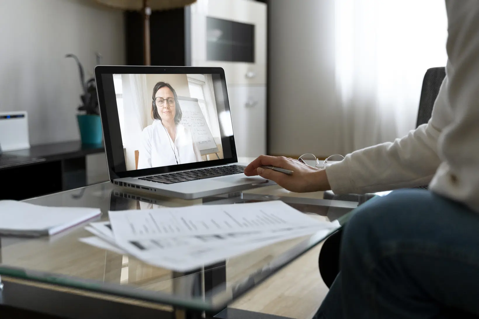 Teleconsulta em andamento: notebook sobre a mesa com a profissional na tela, documentos e gráficos impressos ao lado